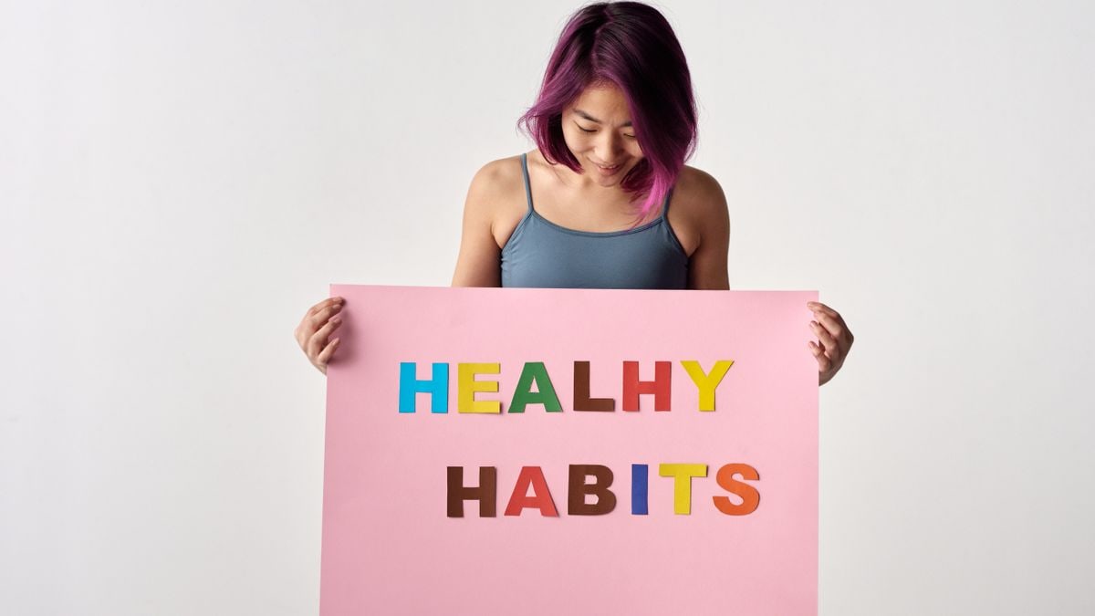 Asian woman holding a colorful 'Healthy Habits' sign in a studio setting, promoting wellness.