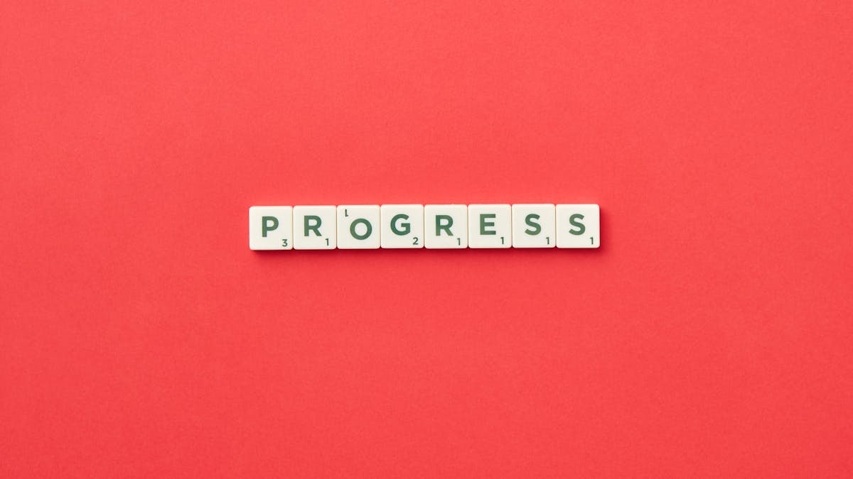 Scrabble tiles spelling 'Progress' on a vibrant red background, symbolizing development.